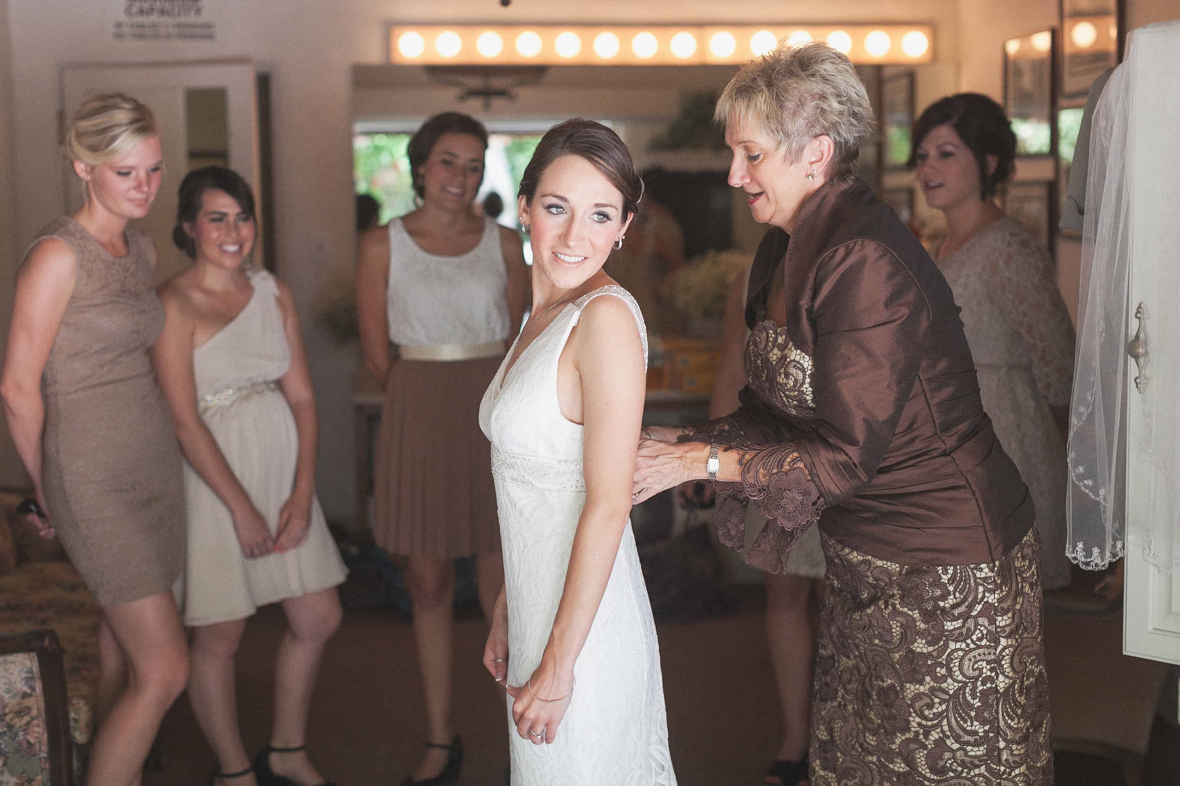 Mother of the Bride helping bride with her dress and guests surrounds them