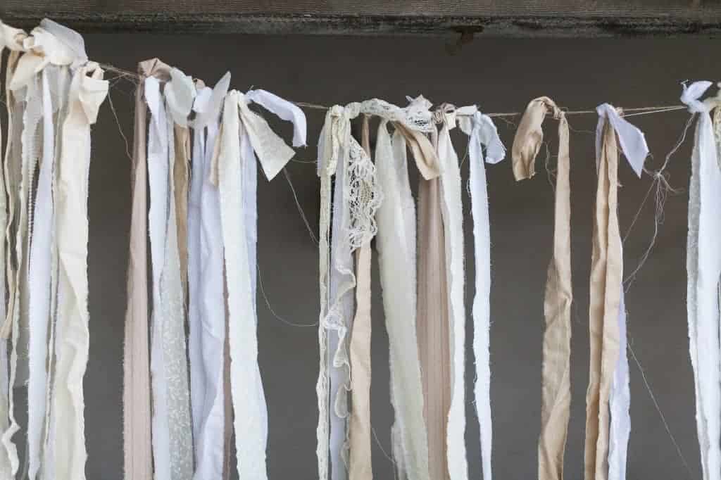 Save money on your wedding decor by using DIY decorations. We made this simple ceremony backdrop with pieces of fabric tied to jute string.