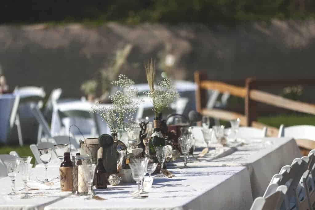 Our wedding dinner tables were decorated with rustic elements like watering cans, vintage bottles, vases, goblets, candles, and more - all bought on sale or borrowed to save money on wedding decor.