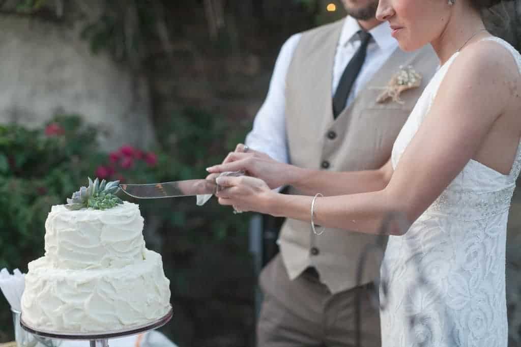 The bride and groom cut into their small, two-tier wedding cake. Save money on your wedding by having a small cut cake, and other dessert options for guests.