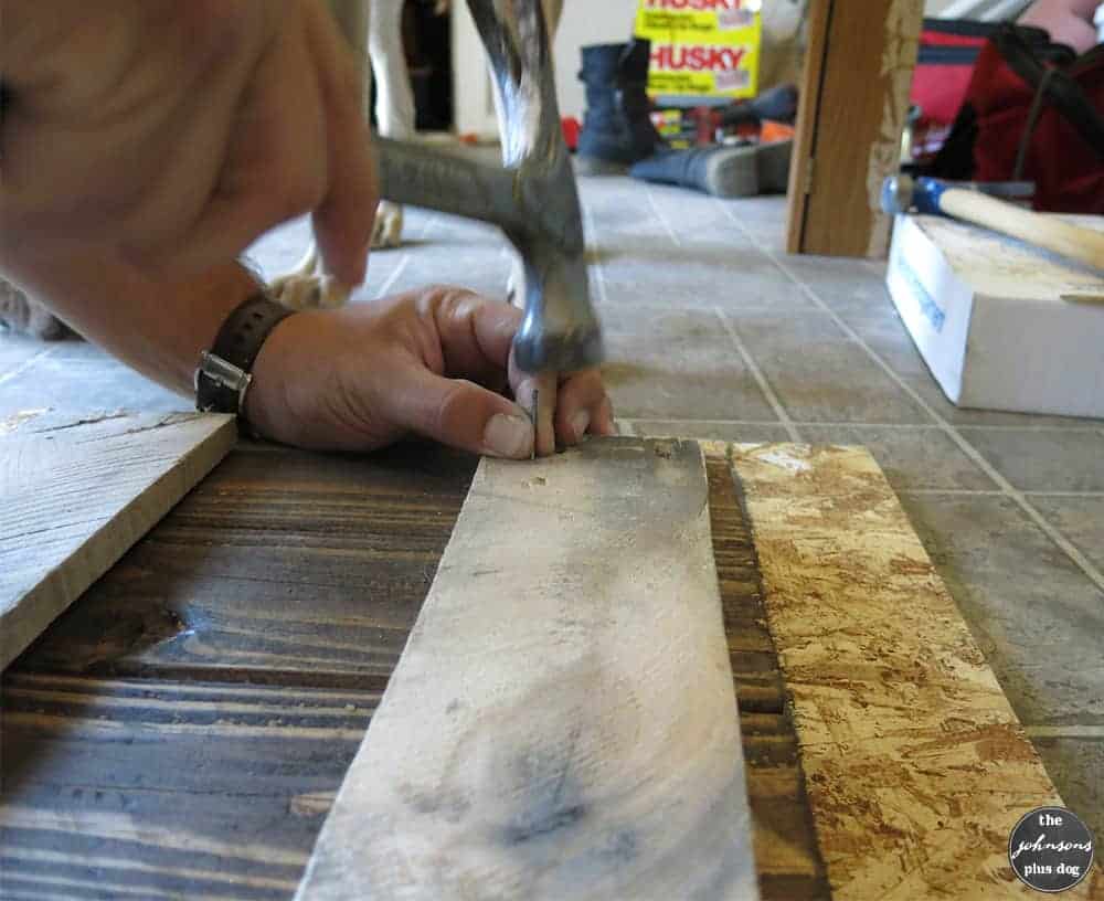 Hammering nails into the support boards on the back of the rustic wood sign.