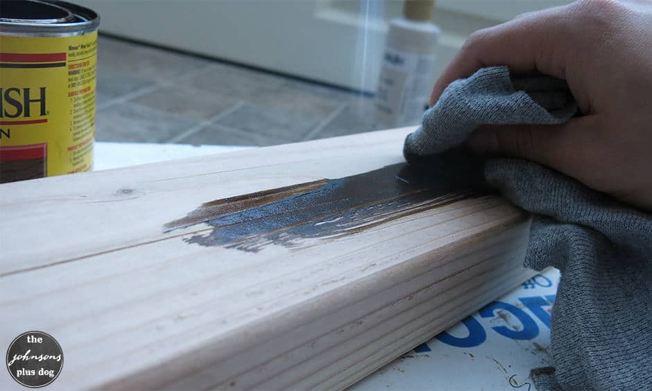 Using a cloth to stain a piece of wood using a dark wood stain.