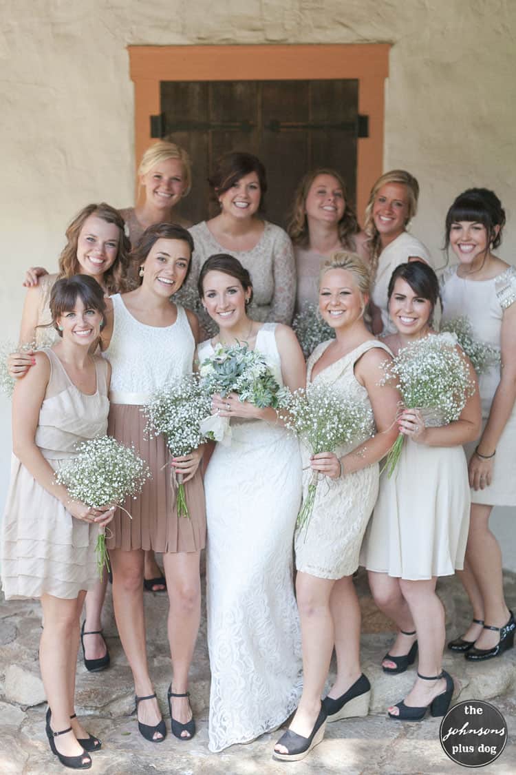 The bride and wedding party from a neutral rustic wedding. The bridesmaids are wearing mismatched dresses and holding baby's breath bouquets.