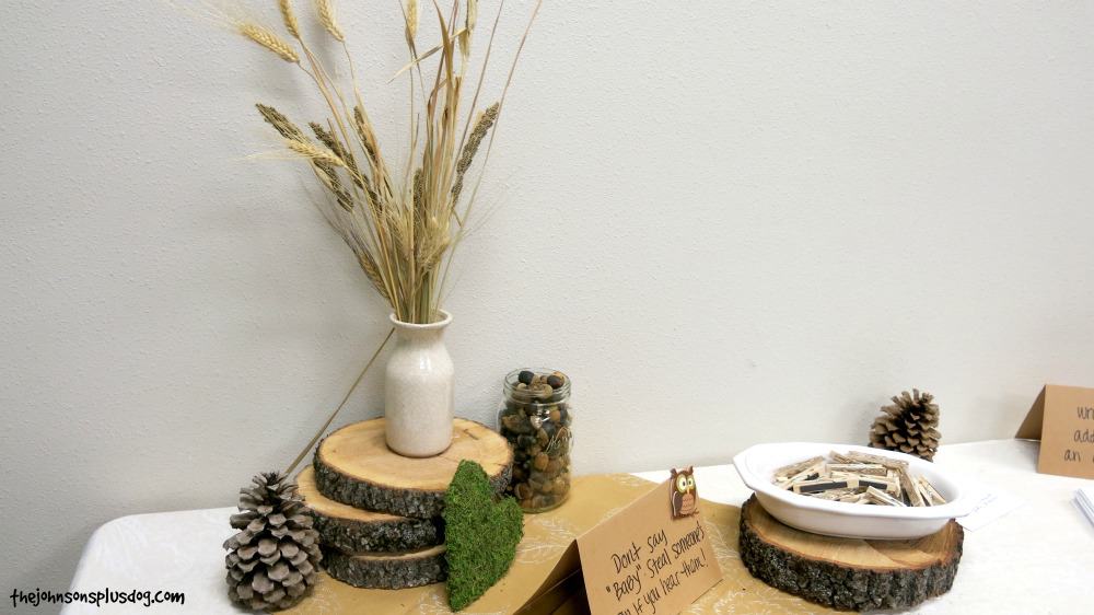 stacked up wood rounds, large pinecones, vases with dried wheat, mason jars full of acorns and neutral table clothes for baby shower table decorations