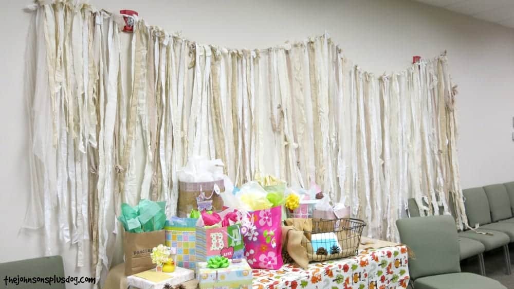 Ripped fabric and lace banner up on the wall behind the gift table at baby shower