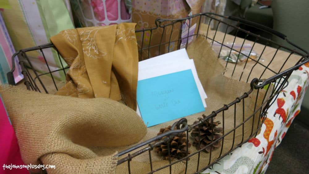 Burlap, cards in envelopes and dried pine cones in the metal basket on the table for gifts at woodland baby shower