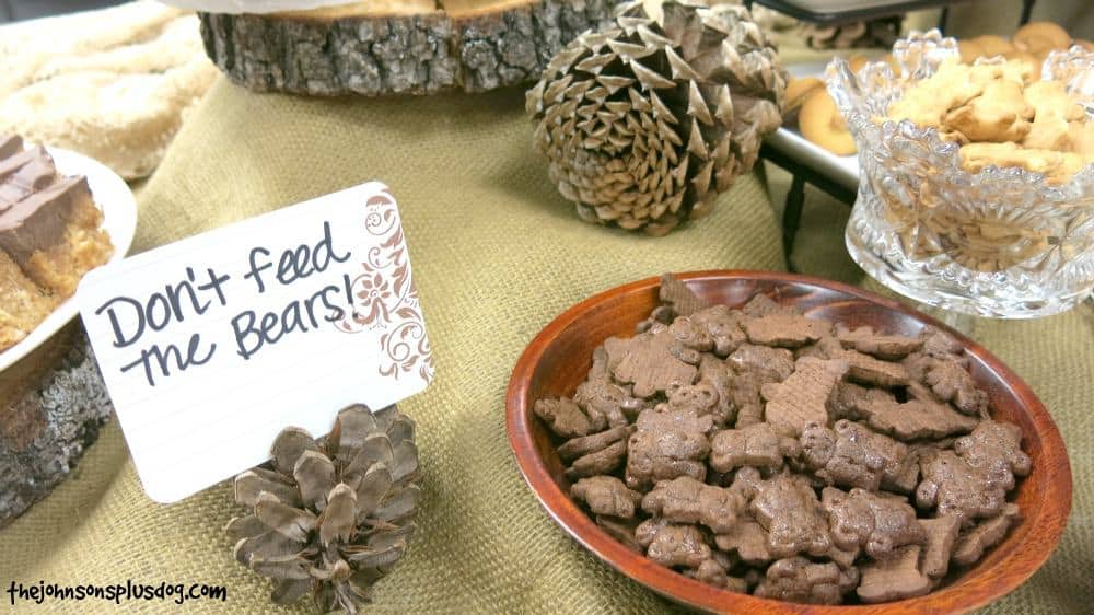 Teddy grahams in wood plate beside card standing in pinecone that says Don't feed the bears