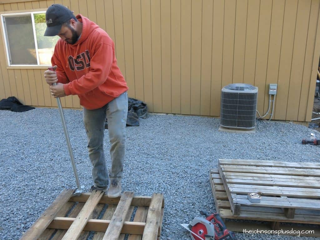 Using a Pallet Buster - a metal pry bar perfect for taking apart wood pallets - to disassemble the pallets to create a wood AC unit cover.