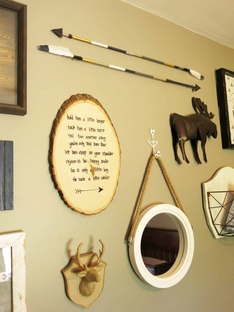 rustic woodland art pieces hung on a wall, including a metal moose, two arrows, a wooden deer head, a small mirror, and a round wooden slab with a poem