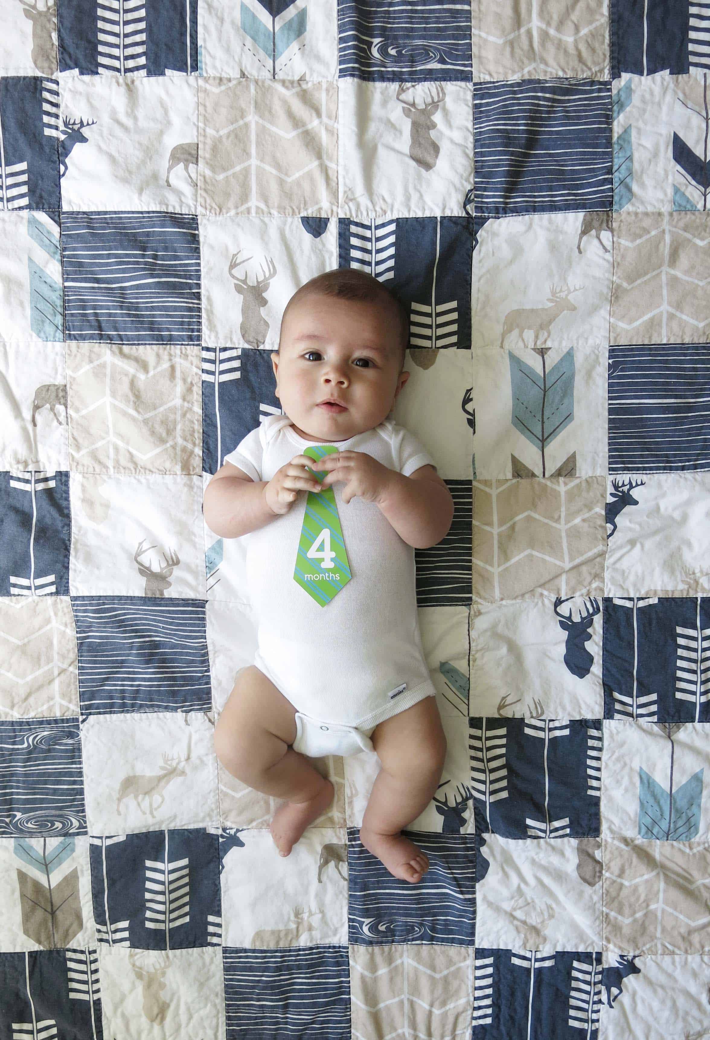 a baby with a tie that says 4 months, laying on a rustic woodland themed blanket