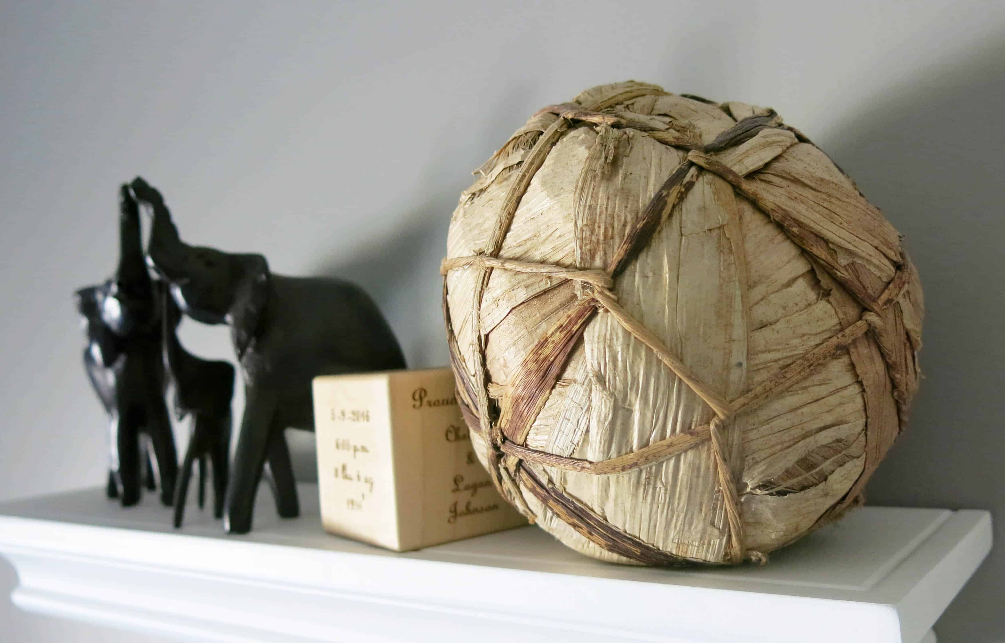 black elephant trinkets, a wooden box, and a rope and corn husk decorative ball on a white shelf