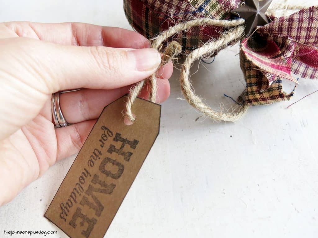 Attaching the stamped decorative Christmas gift tag to the homemade fabric ornament using jute twine.