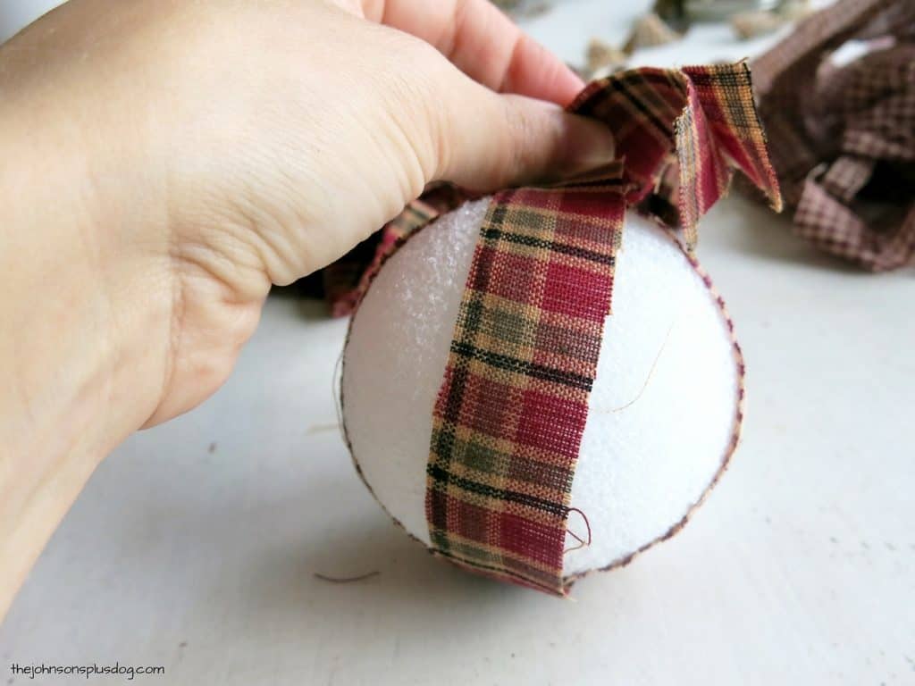 Wrapping strips of homespun fabric around a foam crafting ball to make homemade fabric ornaments.