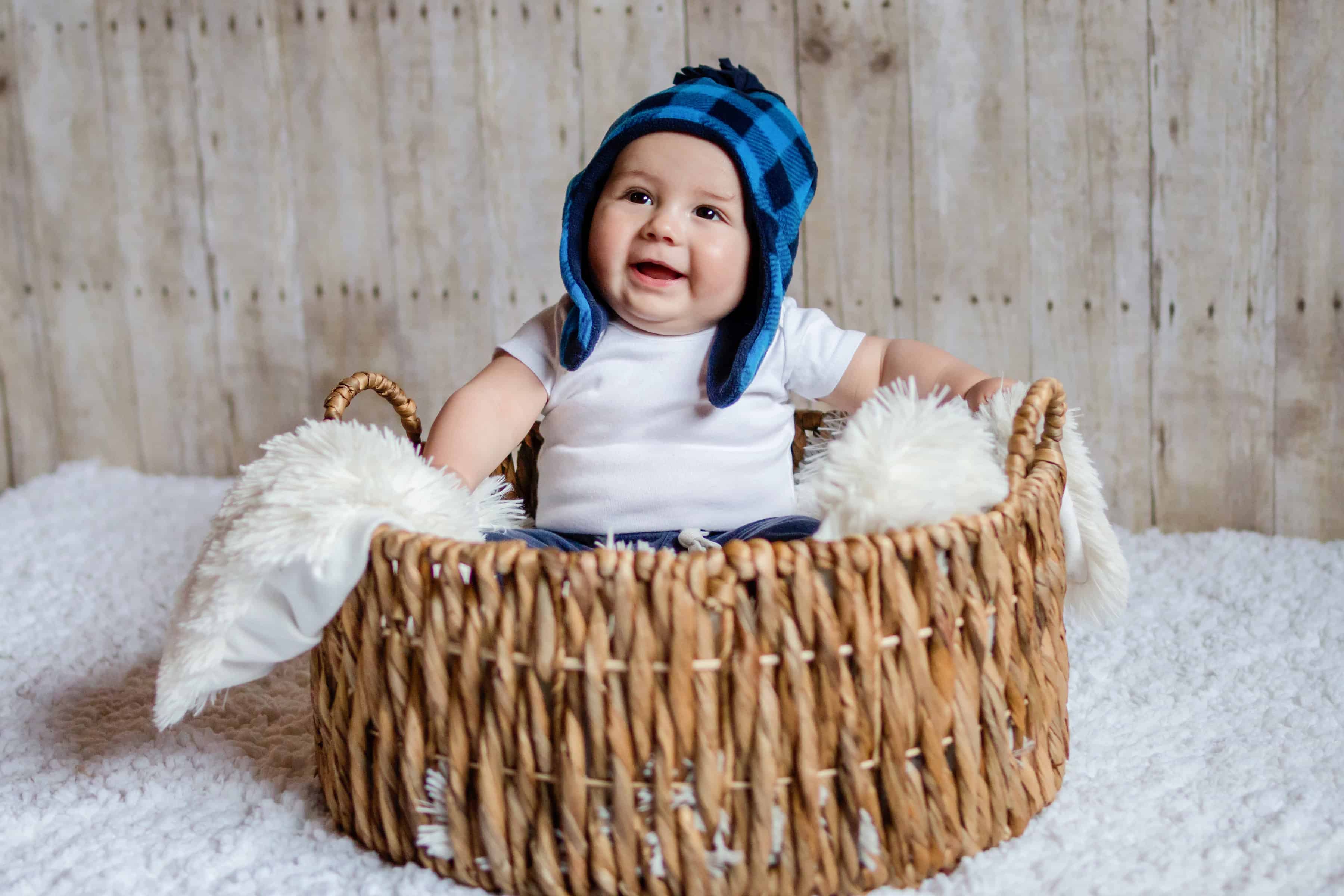 Baby christmas / winter photo showing 6 month old boy wearing blue beanie sitting in basket with wood background