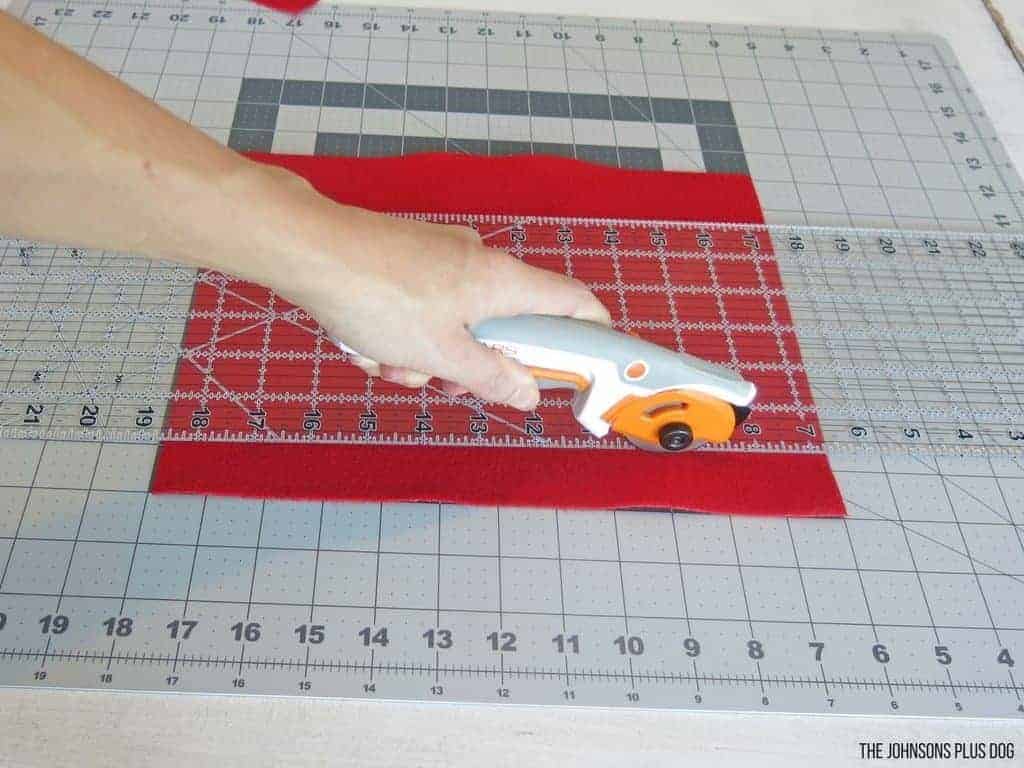 Woman hand holding a rotary cutter cutting red felt on top of cutting mat