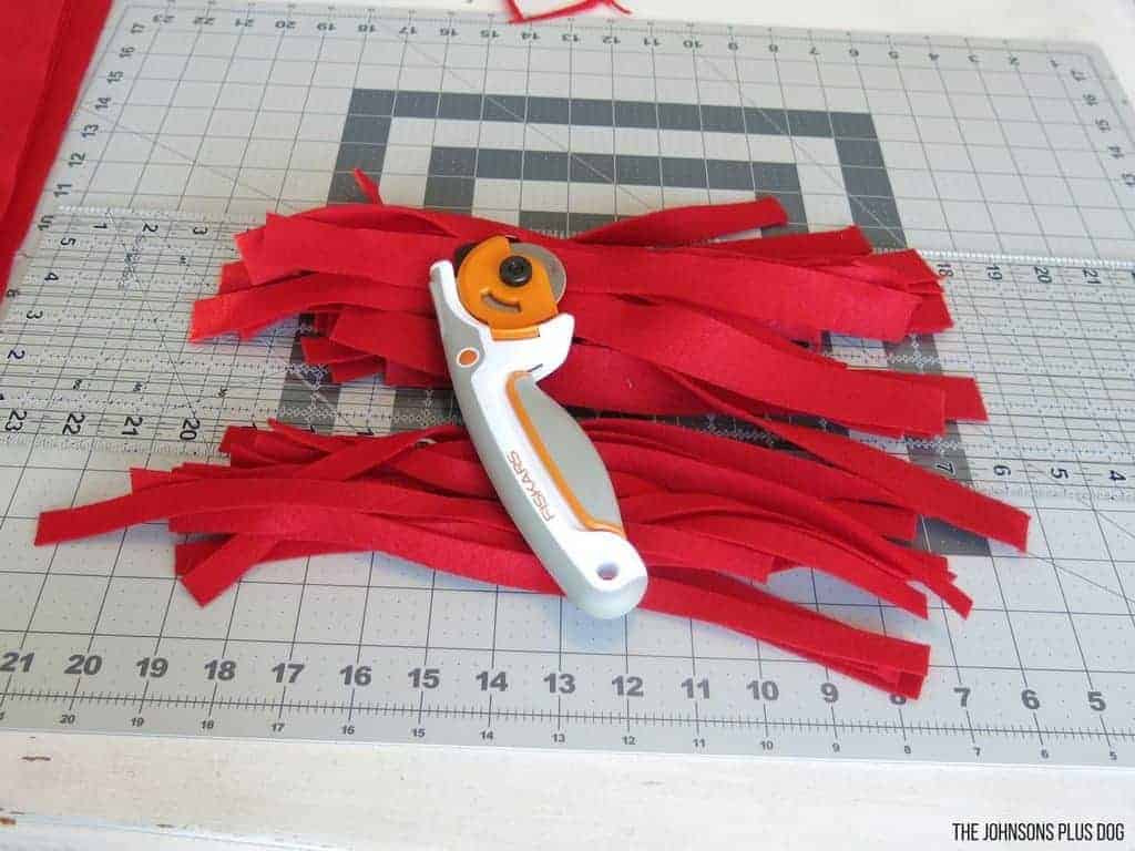 Red felt strips and rotary cutter laying on the cutting mat