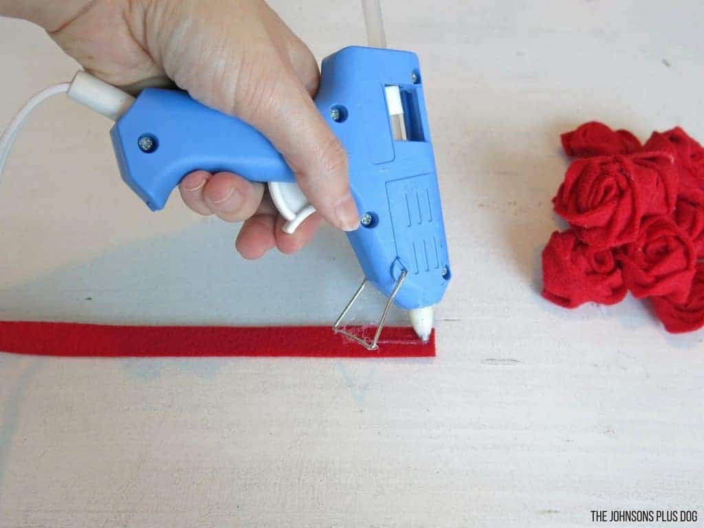 Woman hand holding a glue gun putting glue on a red felt strip beside some crumpled felt strips 