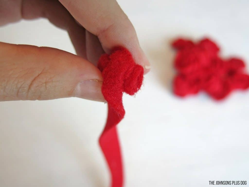 Woman hand rolling the red felt strip into mini rosette flower for Valentine's Day wreath