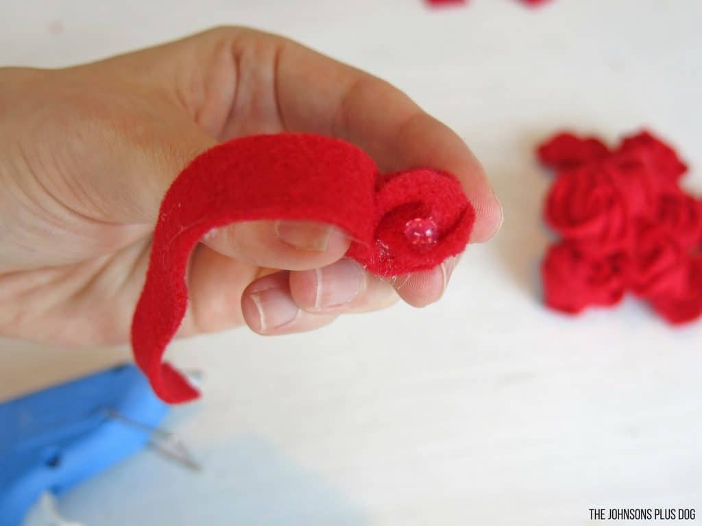 Woman hand rolling the red felt strip nearly on the end of the strip for Valentine's Day wreath