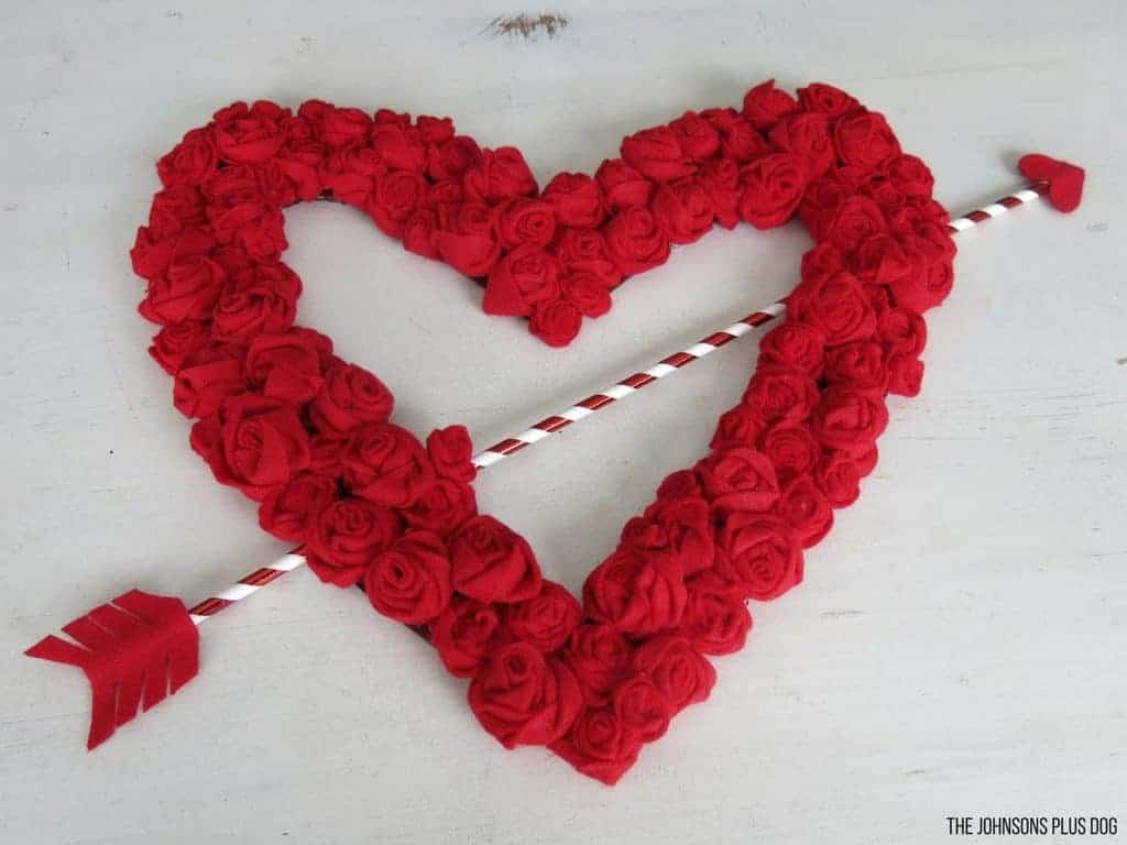 Felt Rosette Valentine's Day Wreath with red and white striped arrow going through the middle laying on a white tabletop