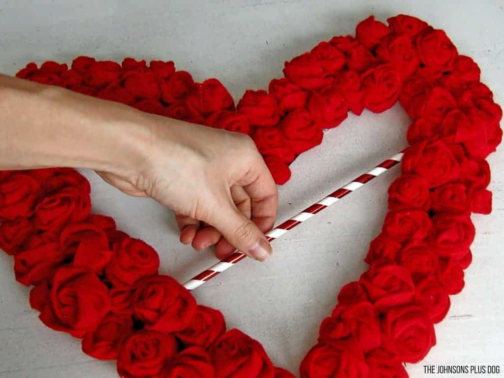 Hand attaching a red and white straw to the middle of a heart shaped rosette wreath