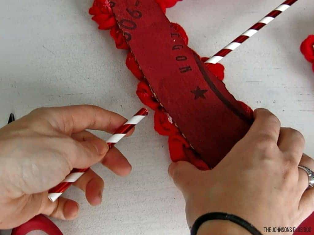 hand holding the rosette wreath facing backwards attaching another white and red straw