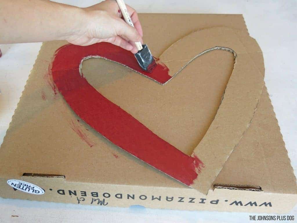 Woman hand holding a foam paint brush painting the heart shaped cardboard with red