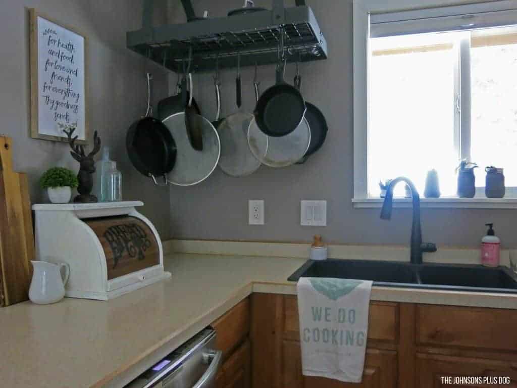 Our chalk-painted vintage bread box sits on a corner of our kitchen counter, next to the sink and hanging pots and pans.