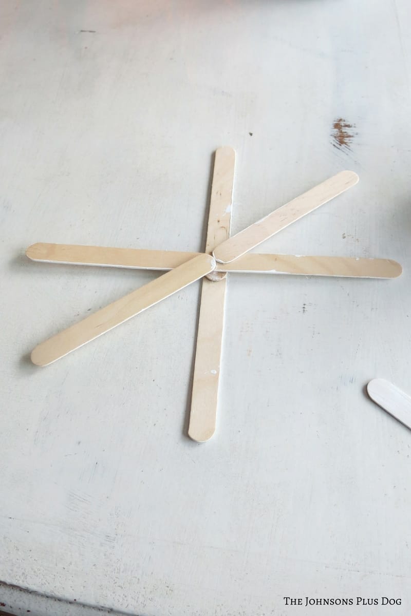 Popsicles sticks attached together forming a snowflake on a white tabletop