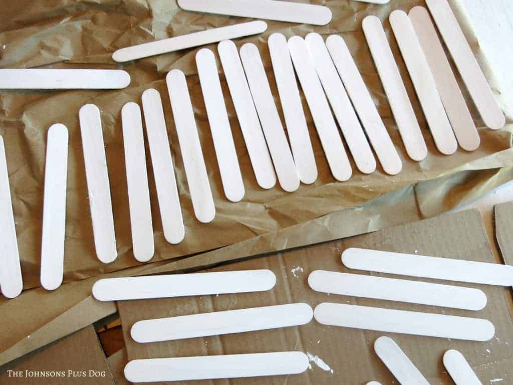 White painted popsicle craft sticks laid on the cardboard