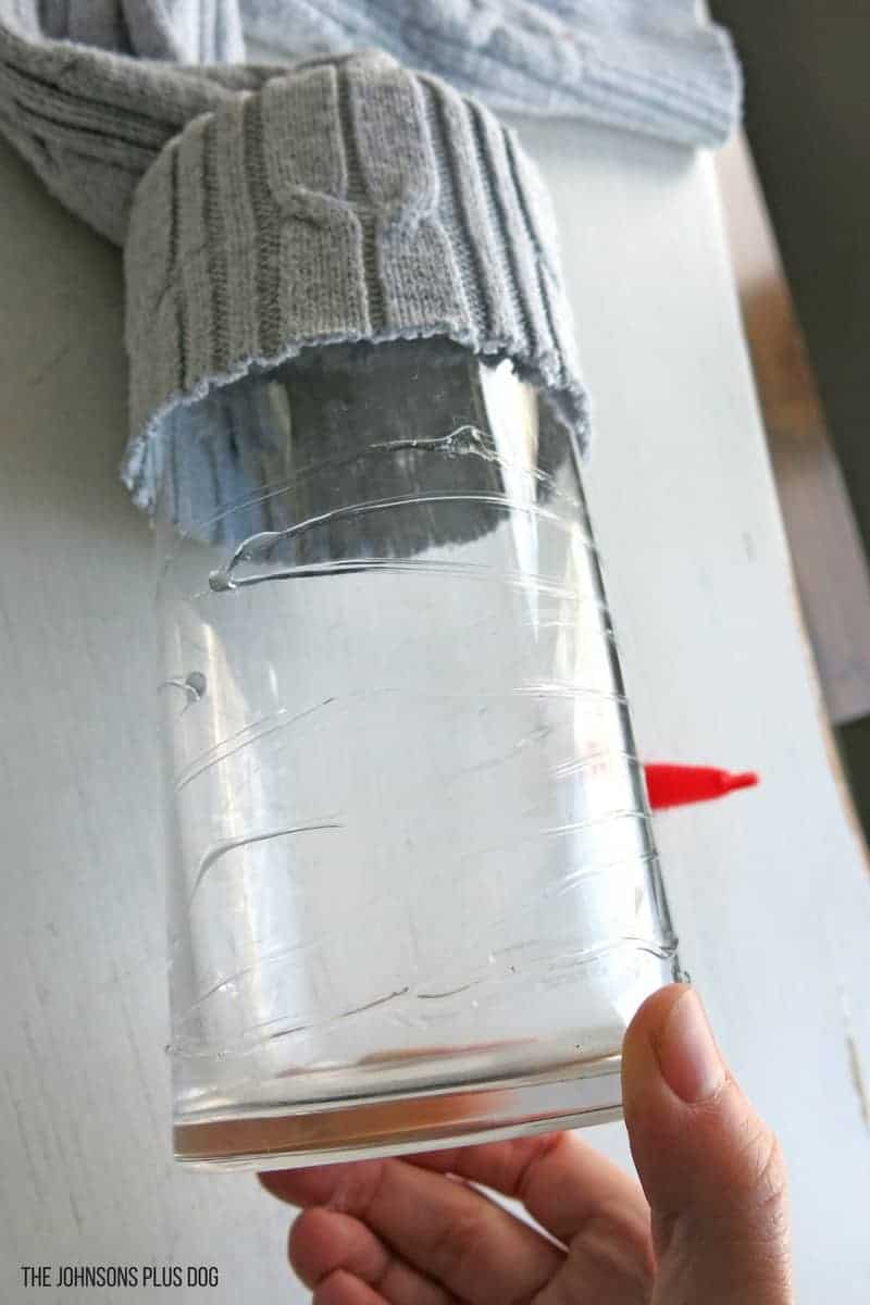 Craft glue applied to a glass vase, with a gray sweater sleeve wrapped around the top of the glass. 