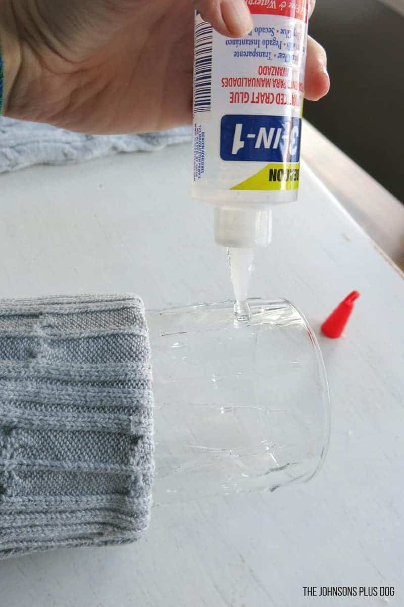 Applying more craft glue to the glass surface of the vase to secure the sweater sleeve.