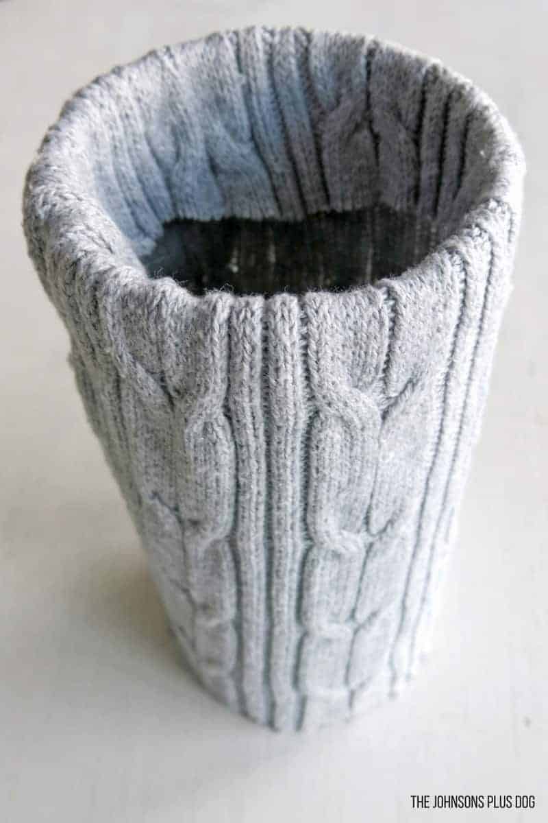 A gray sweater covered vase, with the end of the sleeve folded over the rim of the vase, creating a cozy sweater wrapped vase for winter decor.