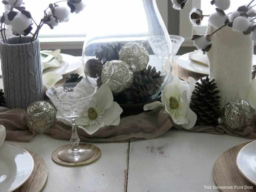 This neutral winter tablescape's centerpiece is created with faux cotton stems and cases with pinecones and flowers