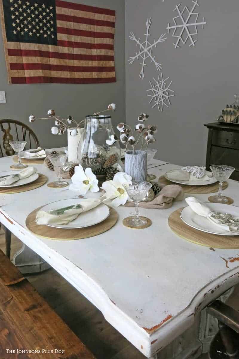 a farmhouse winter tablescape with cotton stem centerpieces and popsicle stick snowflakes on the wall.