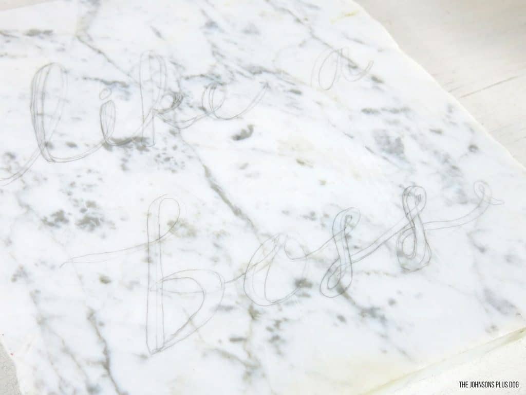 To make this glam office decor, use a pencil to draw on a stencil of whatever words or phrase you want painted on the marble slab. I outlined 