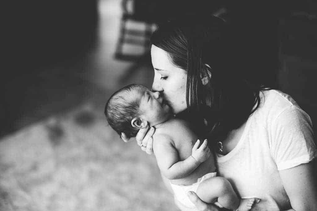 Black and white image of mother kissing newborn baby that is wearing a diaper and crying