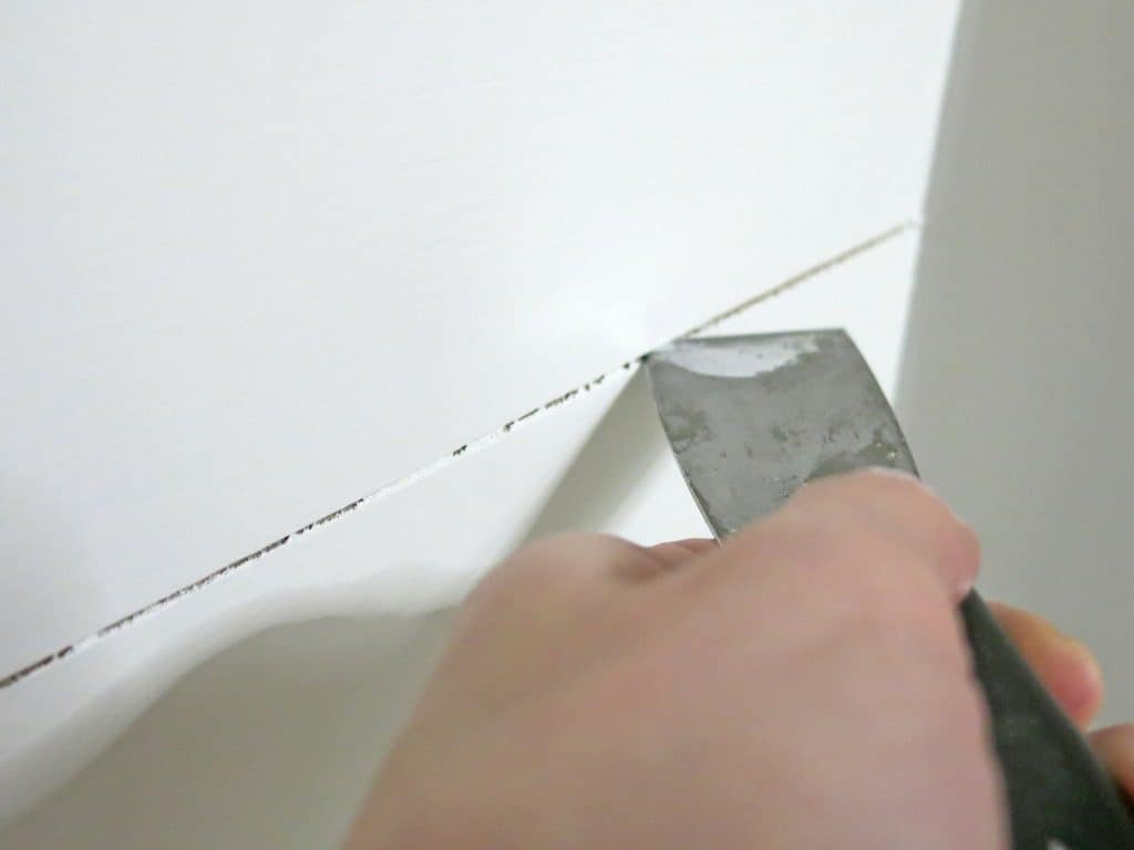 Using a putty knife to scrape the paint from the small cracks between the shiplap planks.