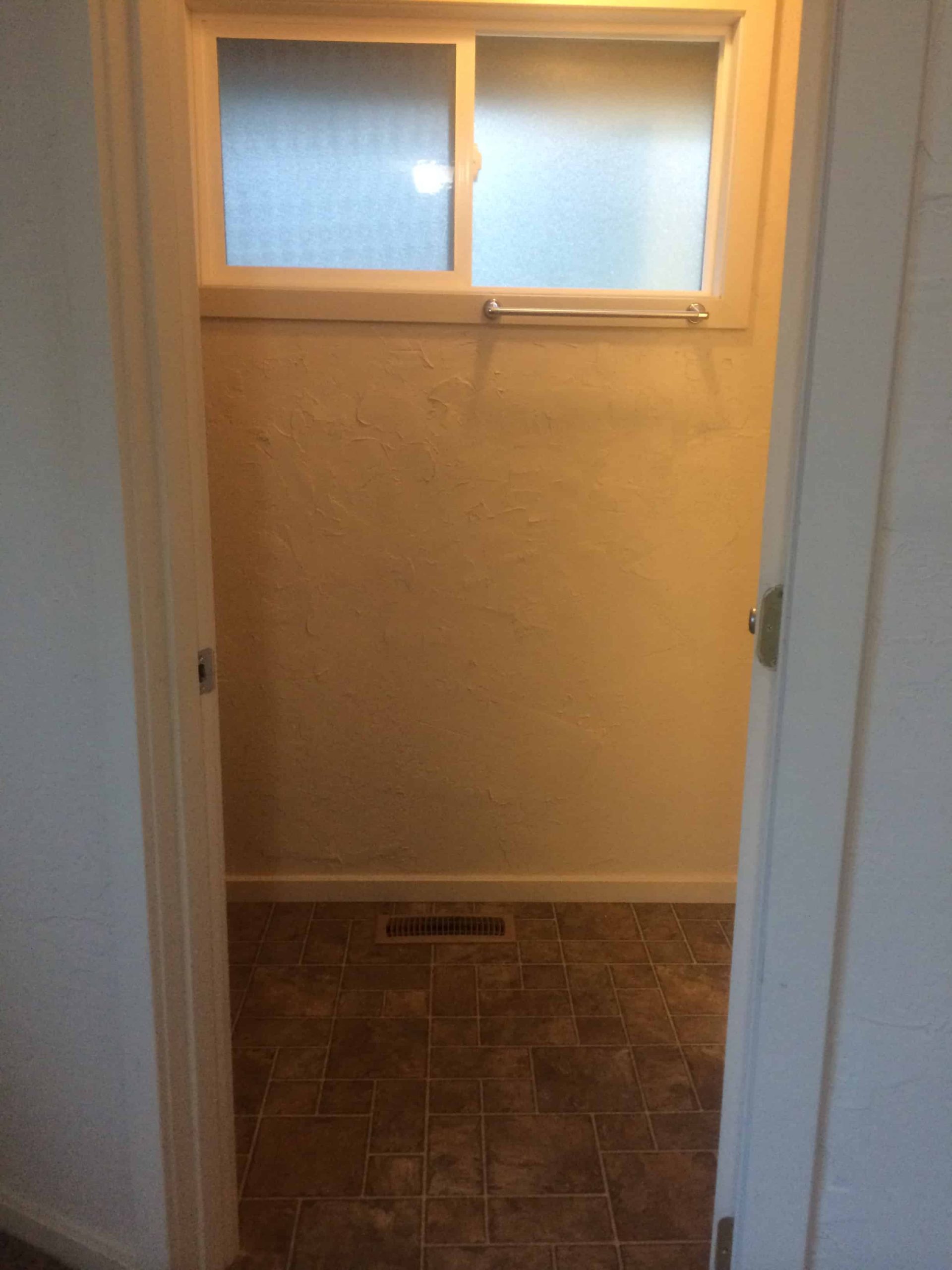 A look at the entrance of our master bathroom shows a small room with stucco walls, dim lighting, and tile floors.