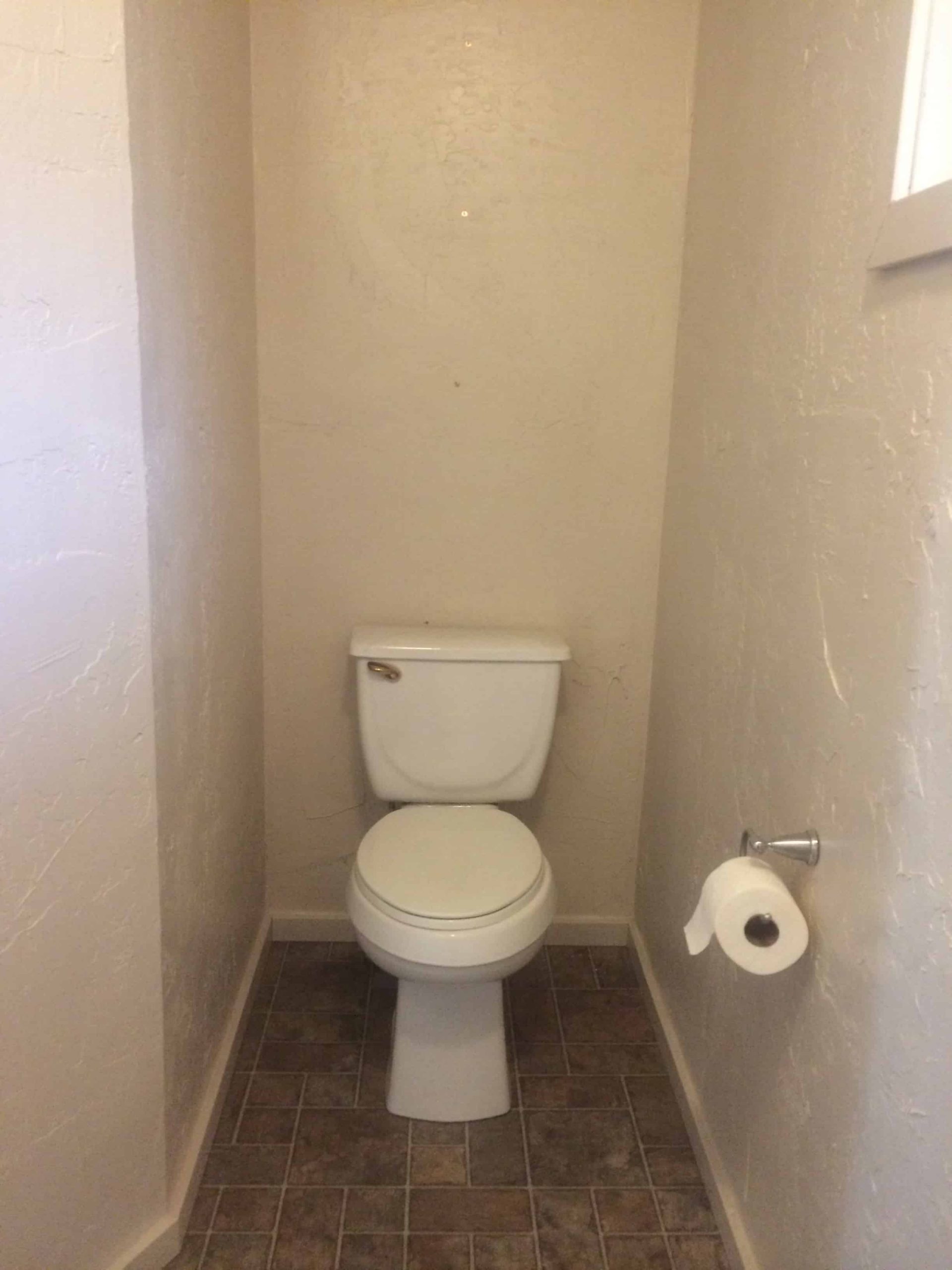 The toilet alcove before renovations was just plain white walls and a plain white toilet, with tile flooring.