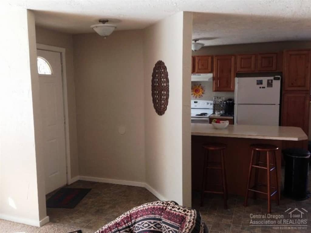 A before photo of a simple home entry way shows a front door and wall dividing the kitchen from the entryway and living room.