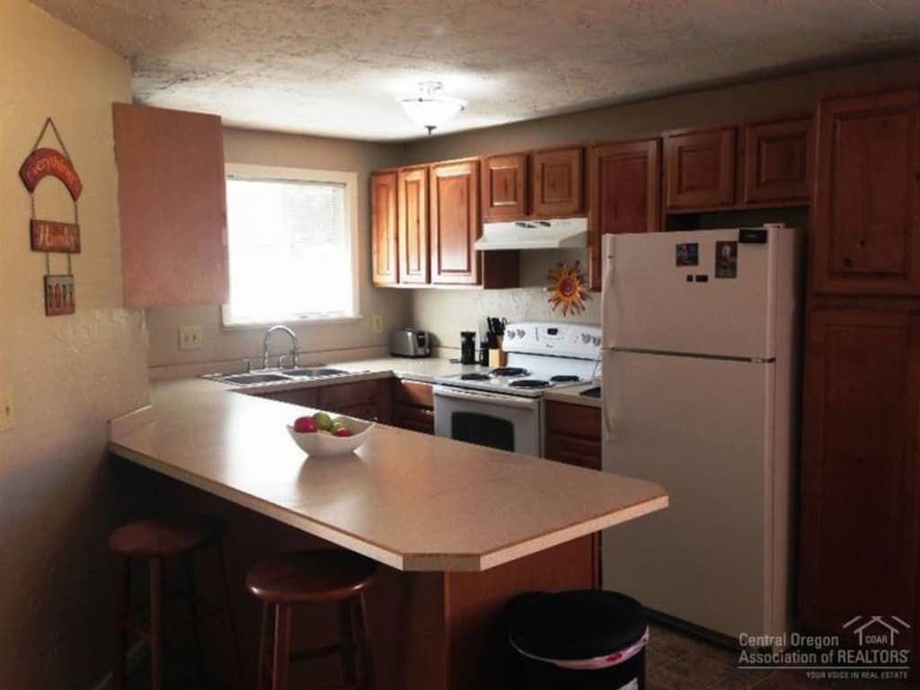 A small, dimly lit kitchen with a breakfast bar, wall of cabinets, and standard kitchen appliances.