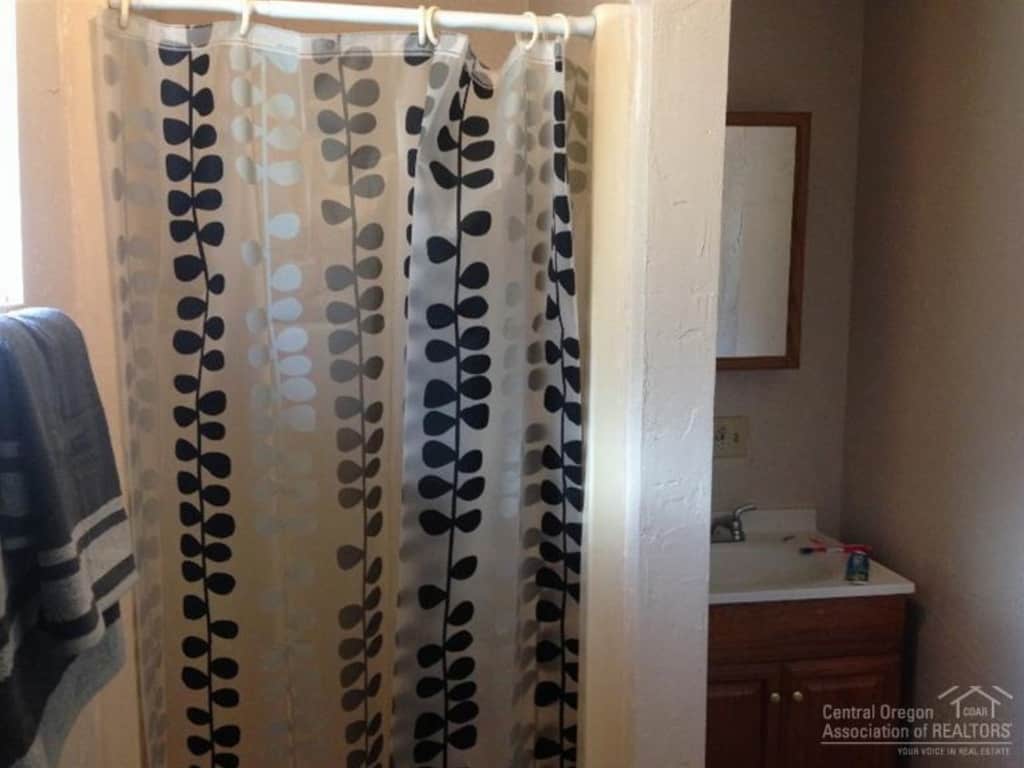 A small walk-in shower, covered with a black and white plastic shower curtain, and small vanity in the master bedroom before renovations.