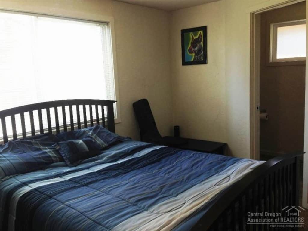 One corner of the master bedroom before renovations, featuring a large bed in front of a window, and the entrance to the master bedroom on the right.