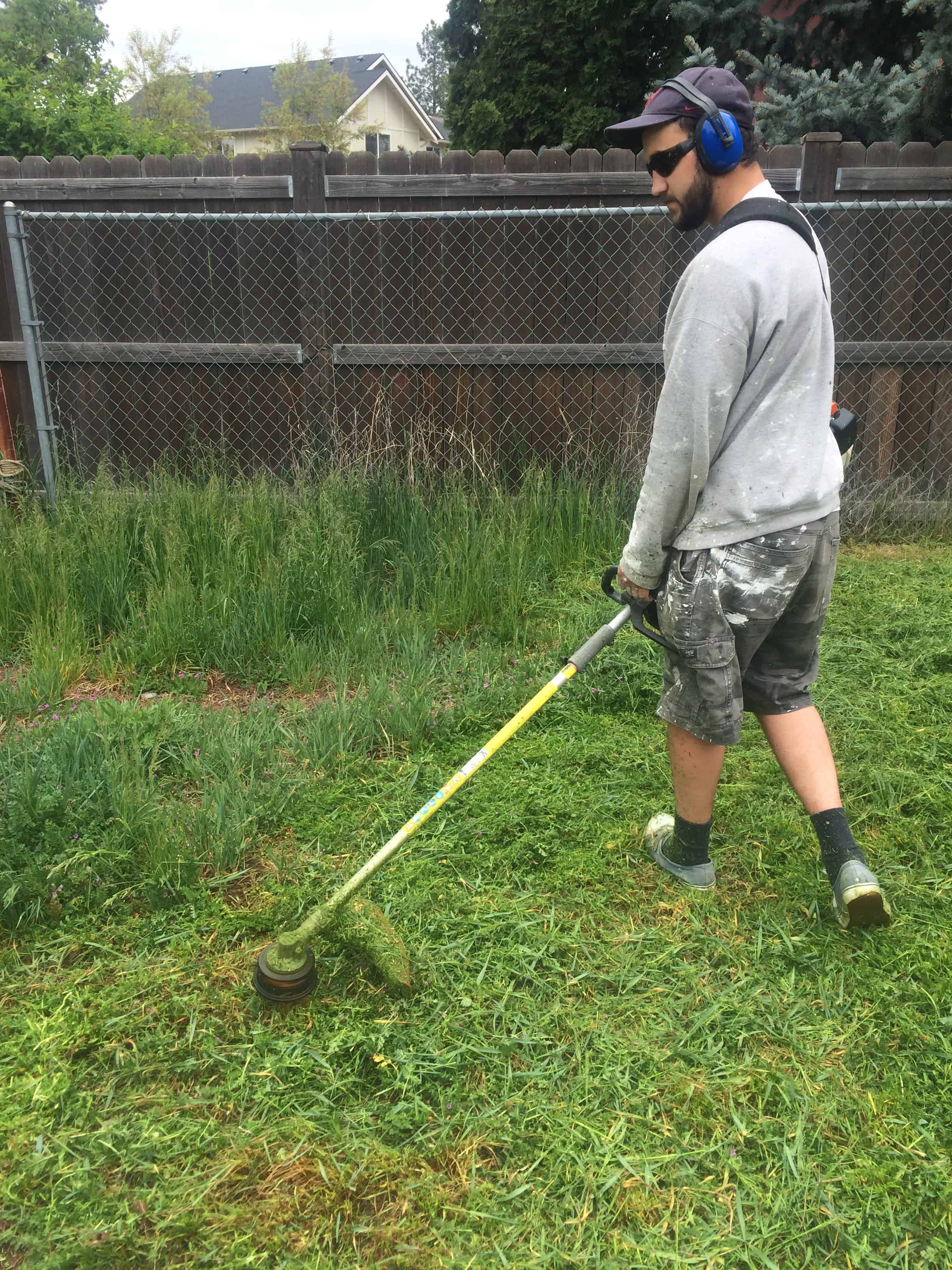 Logan using the weed wacker to control the overgrown weeds taking over our fixer upper's back yard.