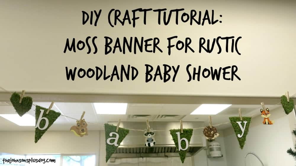 A DIY rustic baby shower banner hangs from a wall. The banner is made with moss flags and pictures of baby woodland animals. Text across the top of the image says 