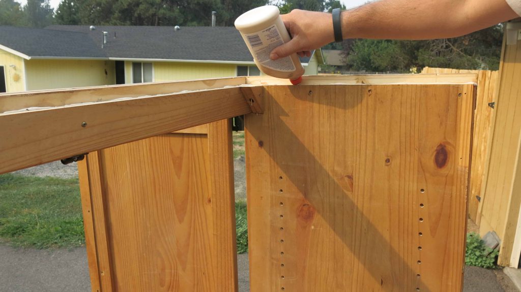 Man's hand adding wood glue to the top of entertainment center to turn into a DIY pantry