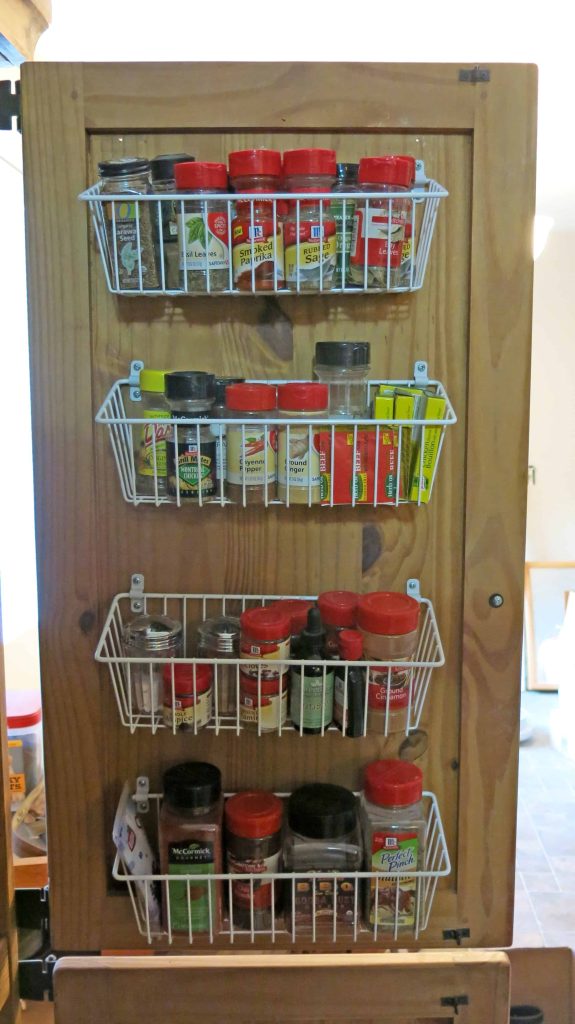 Open door on cabinet turned into a pnatry with white wire baskets attached to door filled with spices