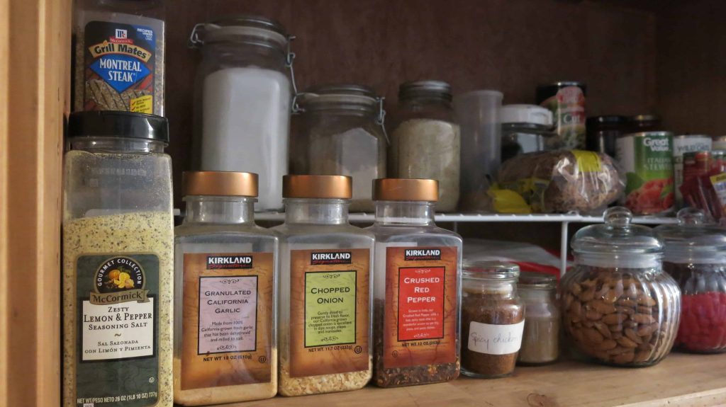 Pantry organization with spices lined up in front of food stacked on wire shelves