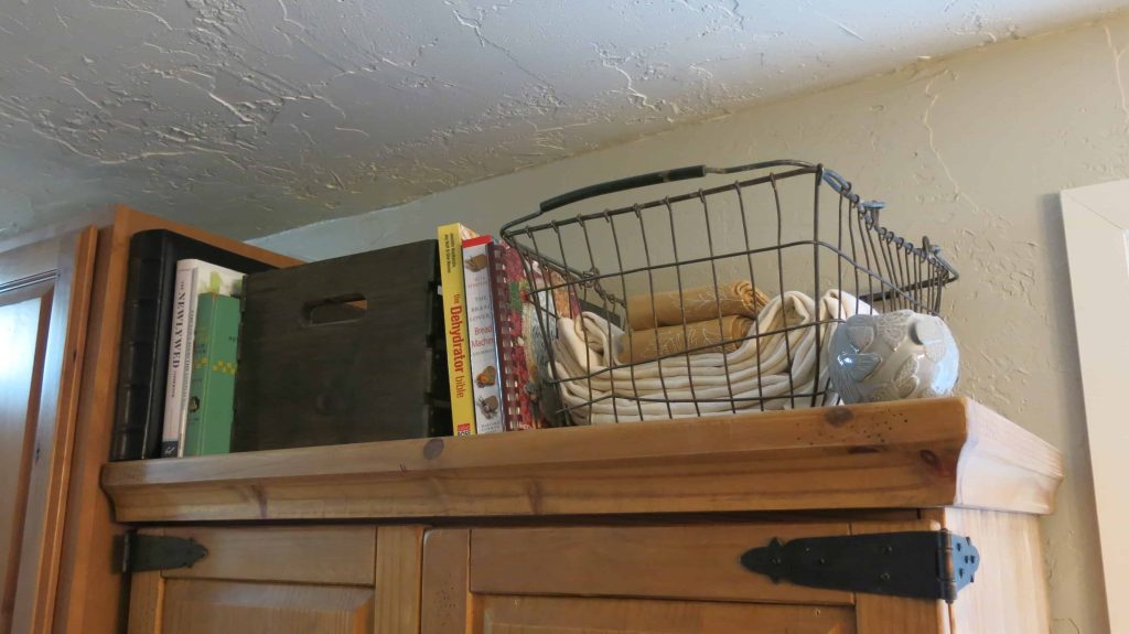 Top of DIY pantry with antique wire basket full of table cloths and cook books stacked on top of cabinet